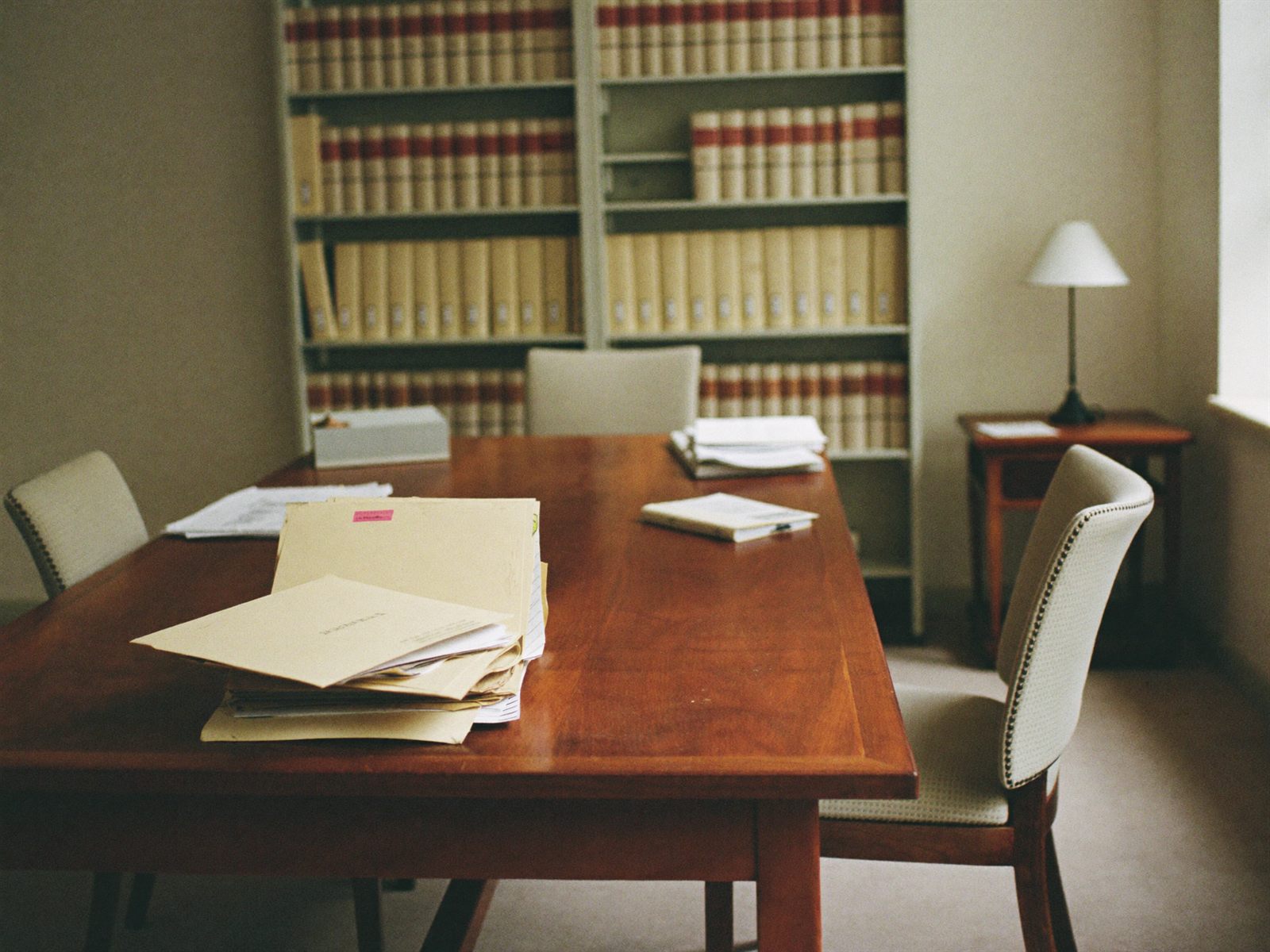 A small law firm meeting room — timber table, stacked client files and shelves of law reports.